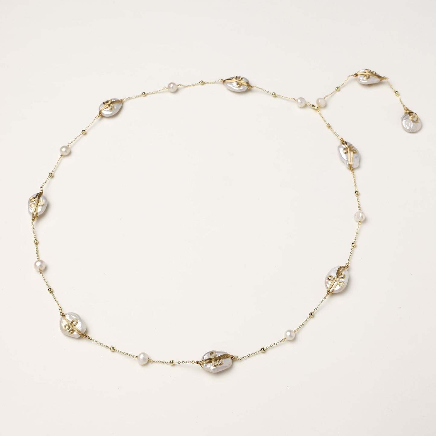 Delicate gold-plated necklace featuring translucent leaf-shaped baroque pearls and round freshwater pearls on neutral background.