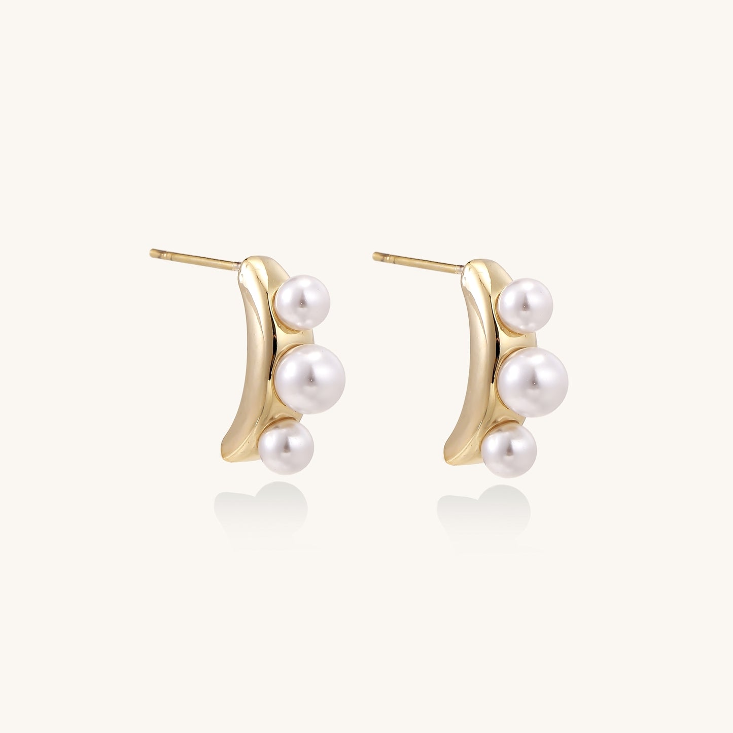 Delicate gold stud earrings with three lustrous white freshwater pearls arranged in an organic curved line.