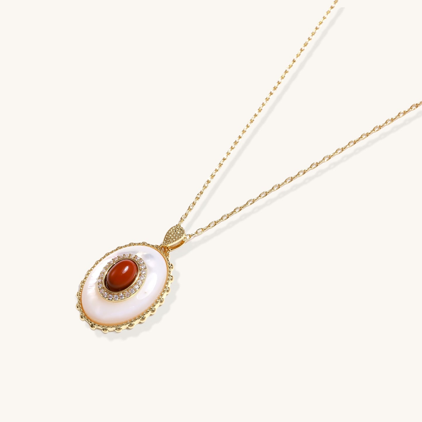 Oval gold-plated pendant featuring mother-of-pearl base with carnelian center stone and crystal accents on delicate chain