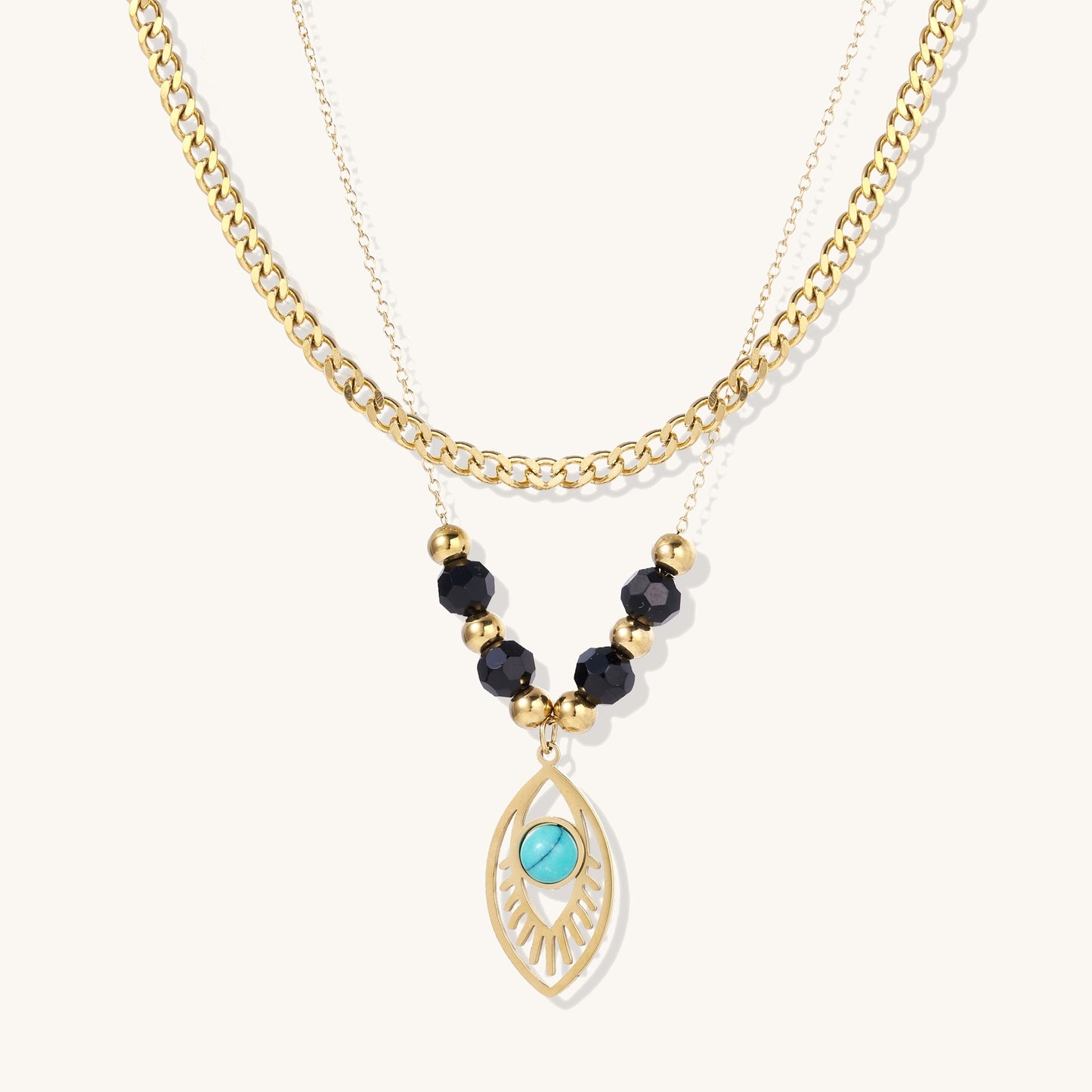 Gold layered necklace set with evil eye pendant, turquoise center stone, and black beaded chain on cream background
