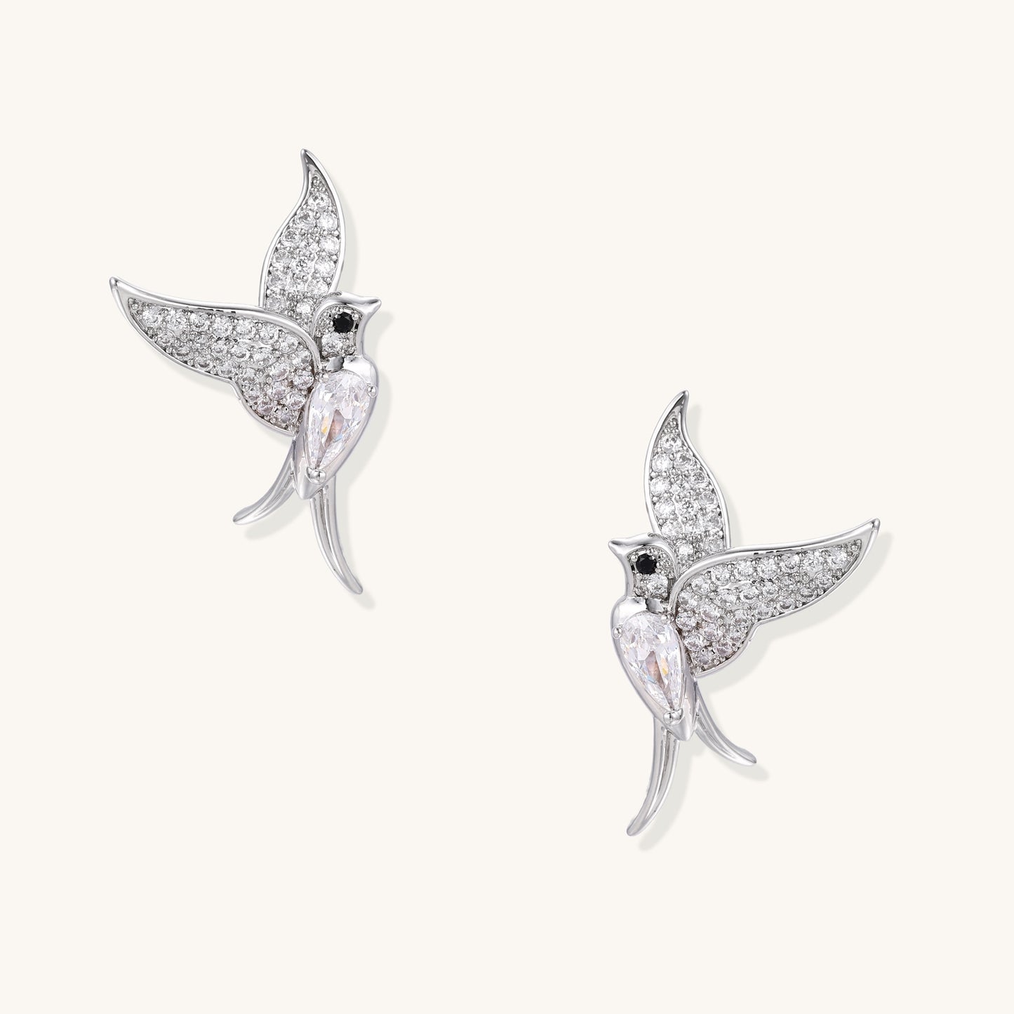 Pair of gold-plated hummingbird earrings with crystal pavé wings and black stone eyes on neutral background.