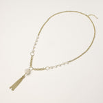 Layered gold-plated necklace with freshwater pearls, central pearl cluster, and chain tassel on cream background.