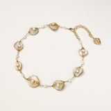 Delicate gold chain bracelet featuring iridescent shell charms with freshwater pearls on white background.