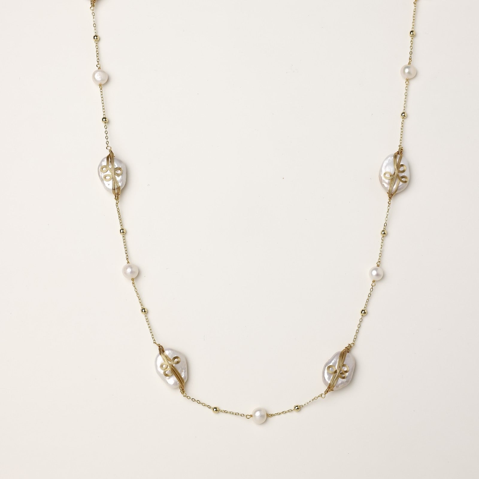 Delicate gold-plated necklace featuring translucent leaf-shaped baroque pearls and round freshwater pearls on neutral background.