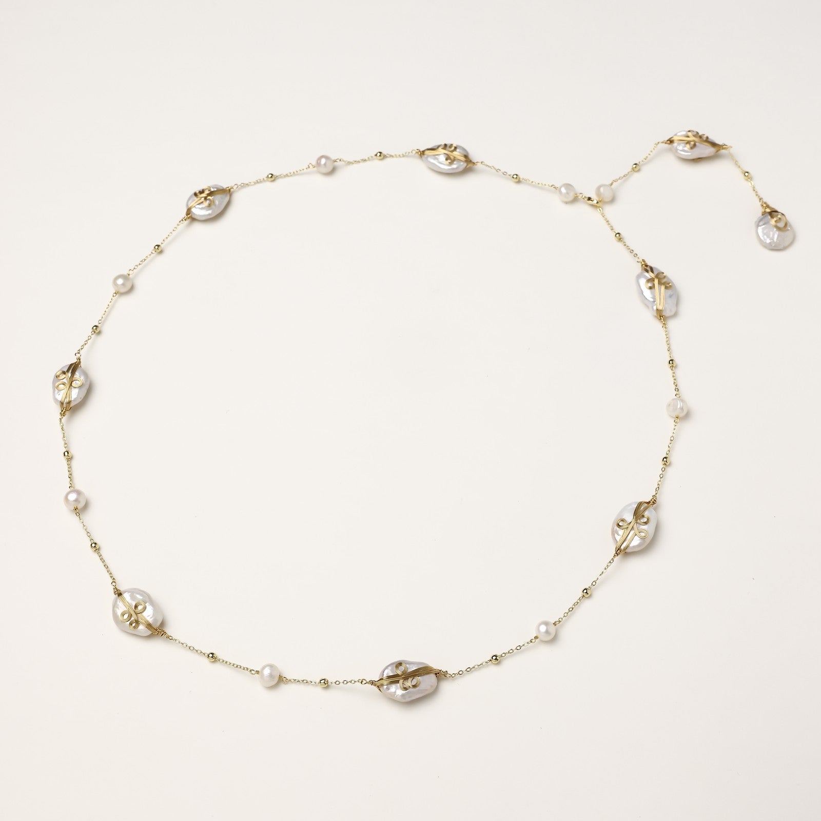 Delicate gold-plated necklace featuring translucent leaf-shaped baroque pearls and round freshwater pearls on neutral background.