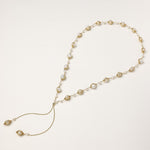 Long gold-plated lariat necklace with wire-wrapped freshwater pearls and chain tassel detail on cream background.