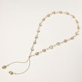Long gold-plated lariat necklace with wire-wrapped freshwater pearls and chain tassel detail on cream background.