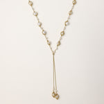 Long gold-plated lariat necklace with wire-wrapped freshwater pearls and chain tassel detail on cream background.