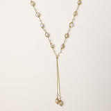 Long gold-plated lariat necklace with wire-wrapped freshwater pearls and chain tassel detail on cream background.