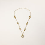 Long gold-plated necklace with eye-shaped elements, freshwater pearls, and baroque pearl pendant on neutral background.