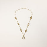 Long gold-plated necklace with eye-shaped elements, freshwater pearls, and baroque pearl pendant on neutral background.