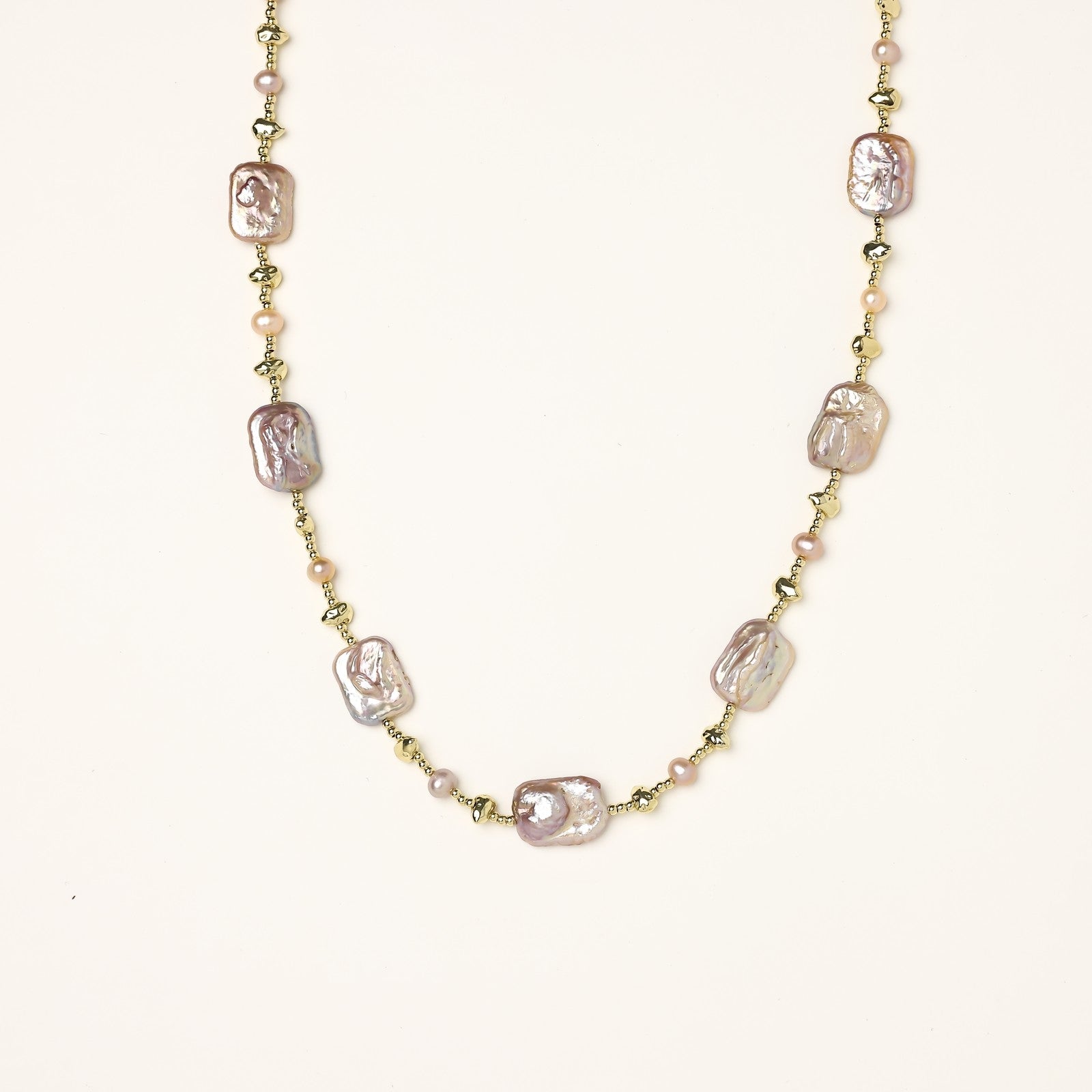 Long gold-plated necklace with iridescent baroque pearls and round freshwater pearls on cream background