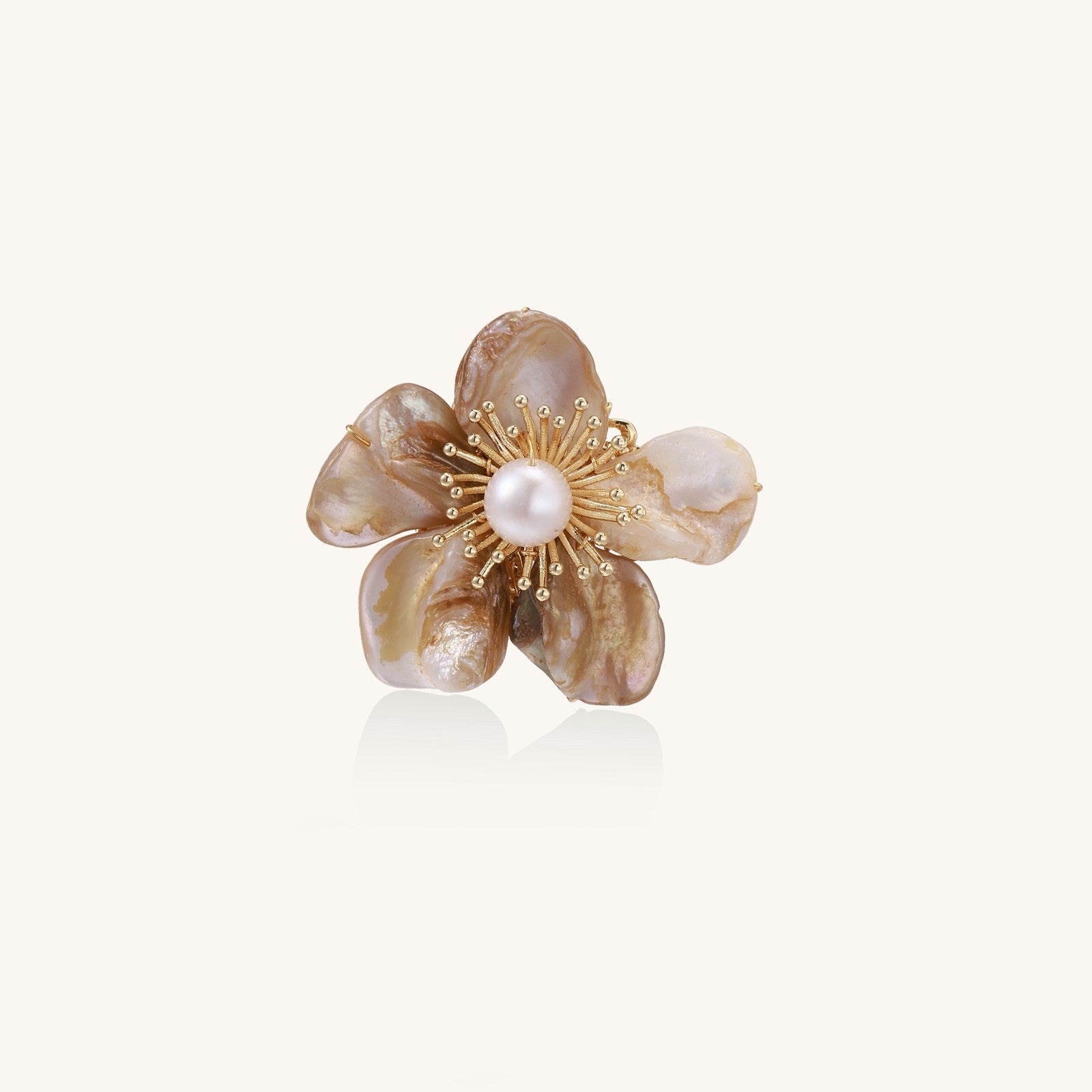 Elegant floral pin with peachy shell petals, gold radiating spokes, and white freshwater pearl center on cream background.