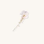 Delicate hair pin featuring translucent shell flower with cascading freshwater pearls on gold chain against cream background.