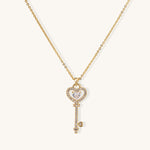 Gold-plated key pendant necklace with heart top and crystal embellishments on adjustable chain against cream background