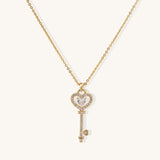 Gold-plated key pendant necklace with heart top and crystal embellishments on adjustable chain against cream background