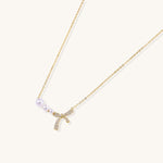 Delicate gold-plated necklace with three white pearls and sparkling bow pendant on cream background.