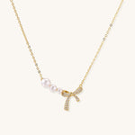 Delicate gold-plated necklace with three white pearls and sparkling bow pendant on cream background.