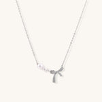 Dainty 14K gold plated necklace with freshwater pearls and sparkling bow charm on white background.