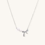 Dainty 14K gold plated necklace with freshwater pearls and sparkling bow charm on white background.