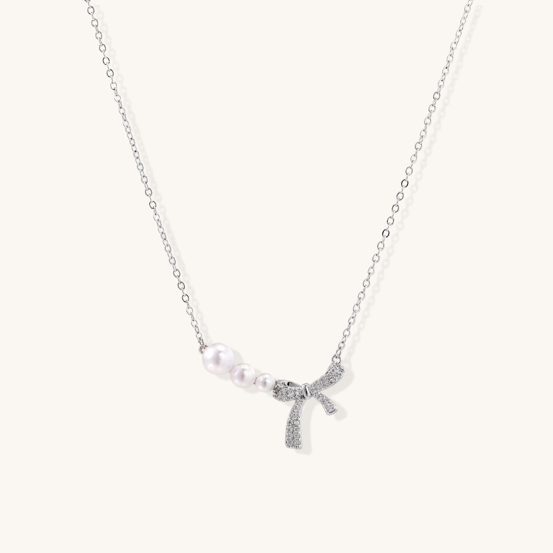 Dainty 14K gold plated necklace with freshwater pearls and sparkling bow charm on white background.