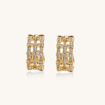 Close-up of geometric gold-plated hoop earrings with crystal pave in intricate lattice pattern on neutral background.