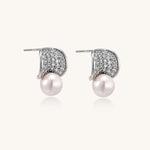 Elegant gold-plated curved earrings with diamond pavé crescents and suspended freshwater pearls on neutral background.
