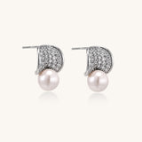 Elegant gold-plated curved earrings with diamond pavé crescents and suspended freshwater pearls on neutral background.