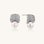 Elegant gold-plated curved earrings with diamond pavé crescents and suspended freshwater pearls on neutral background.