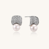 Elegant gold-plated curved earrings with diamond pavé crescents and suspended freshwater pearls on neutral background.