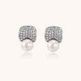 Elegant gold-plated curved earrings with diamond pavé crescents and suspended freshwater pearls on neutral background.