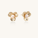 Gold-plated flower stud earrings with freshwater pearl centers on beige background, showing textured petal details.