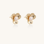 Gold-plated flower stud earrings with freshwater pearl centers on beige background, showing textured petal details.