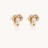 Gold-plated flower stud earrings with freshwater pearl centers on beige background, showing textured petal details.