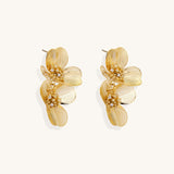 Layered gold-plated floral stud earrings with textured petals and crystal-accented centers on white background.