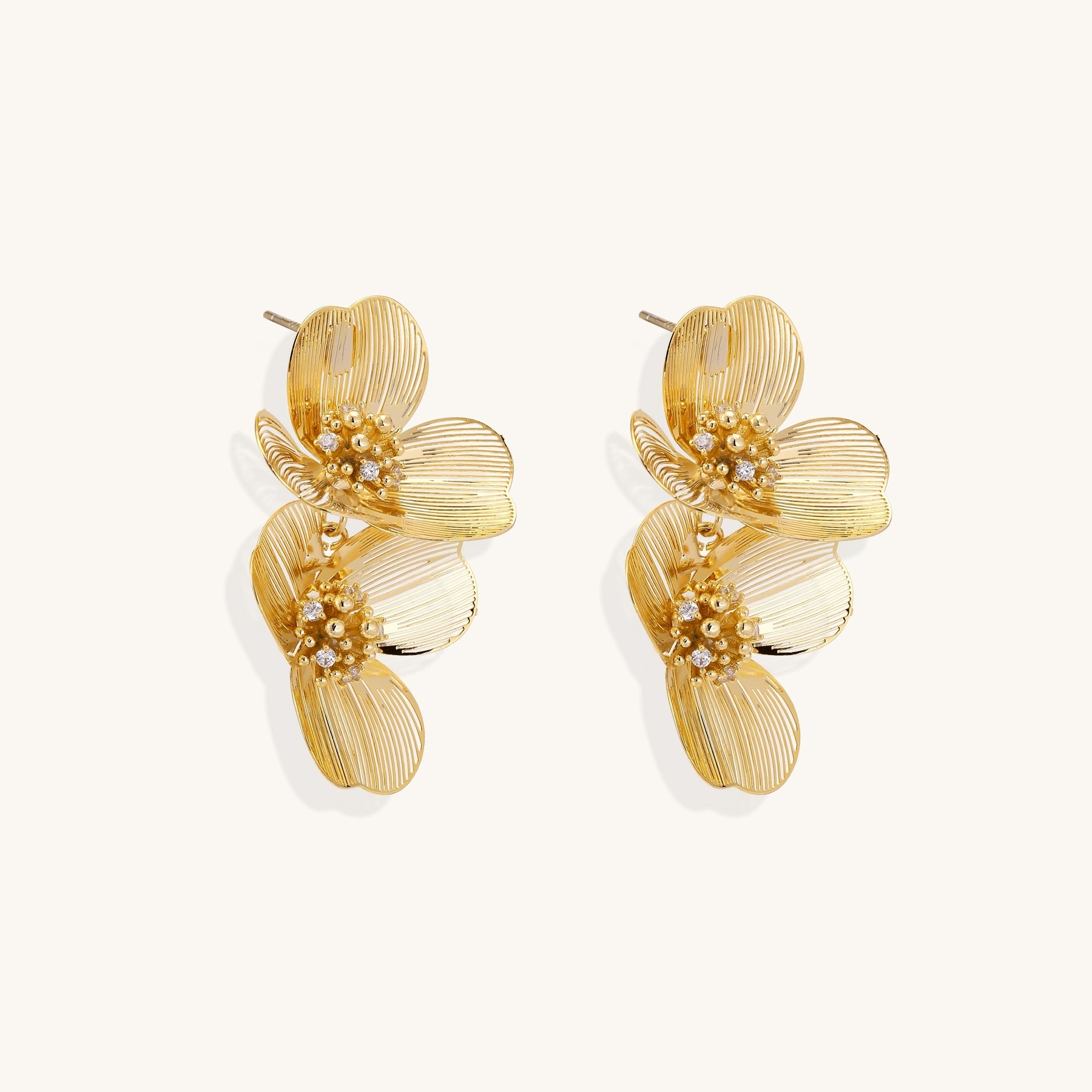 Layered gold-plated floral stud earrings with textured petals and crystal-accented centers on white background.