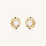 Close-up of gold-plated circular earrings with white mother-of-pearl centers and green zirconia accents on cream background.
