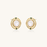 Close-up of gold-plated circular earrings with white mother-of-pearl centers and green zirconia accents on cream background.