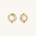 Close-up of gold-plated circular earrings with white mother-of-pearl centers and green zirconia accents on cream background.