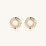 Close-up of gold-plated circular earrings with white mother-of-pearl centers and green zirconia accents on cream background.