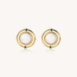 Close-up of gold-plated circular earrings with white mother-of-pearl centers and green zirconia accents on cream background.