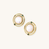 Close-up of gold-plated circular earrings with white mother-of-pearl centers and green zirconia accents on cream background.