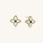 Dainty gold-plated quatrefoil stud earrings with white mother-of-pearl petals and green gemstone centers on beige background.