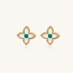 Dainty gold-plated quatrefoil stud earrings with white mother-of-pearl petals and green gemstone centers on beige background.