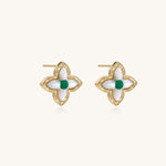 Dainty gold-plated quatrefoil stud earrings with white mother-of-pearl petals and green gemstone centers on beige background.