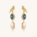 Gold-plated bird dangle earrings with iridescent abalone shell discs and champagne crystal drops on white background.