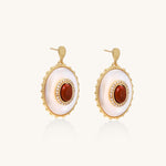 Gold-plated drop earrings with oval mother-of-pearl stones, central red gemstones, and crystal accents on white background.