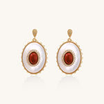 Gold-plated drop earrings with oval mother-of-pearl stones, central red gemstones, and crystal accents on white background.