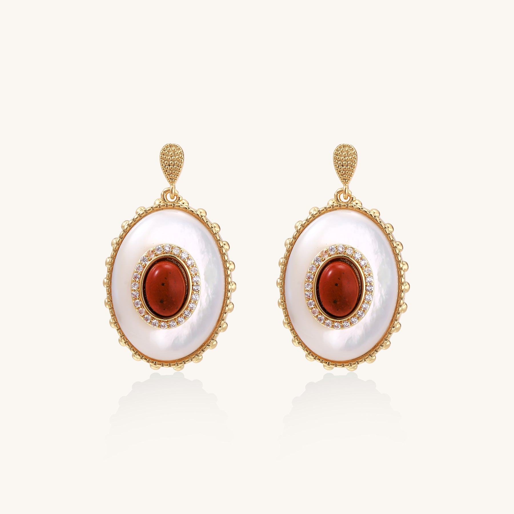 Gold-plated drop earrings with oval mother-of-pearl stones, central red gemstones, and crystal accents on white background.