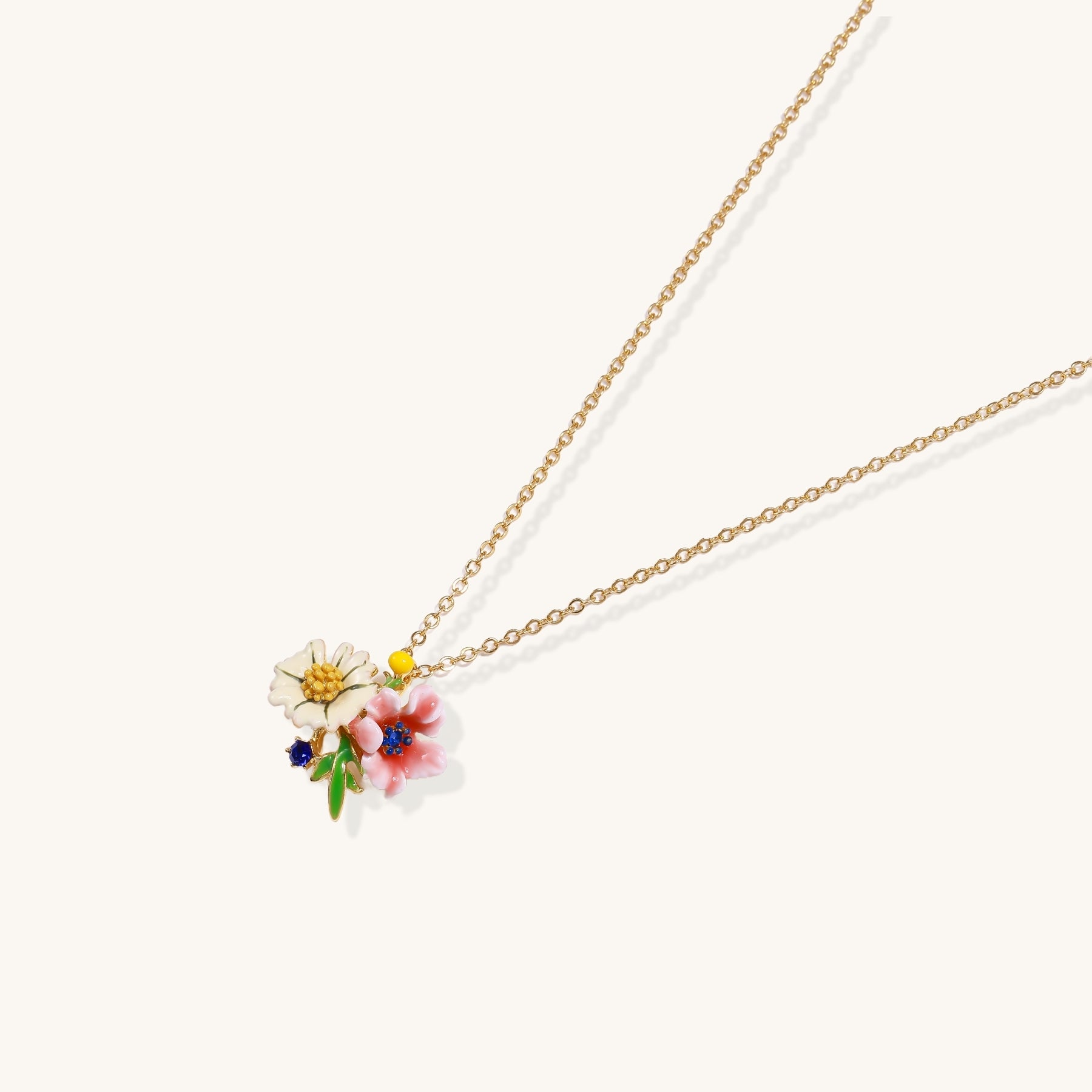 Delicate gold-plated necklace featuring white daisy and pink flower enamel pendant with colorful accents on white background.